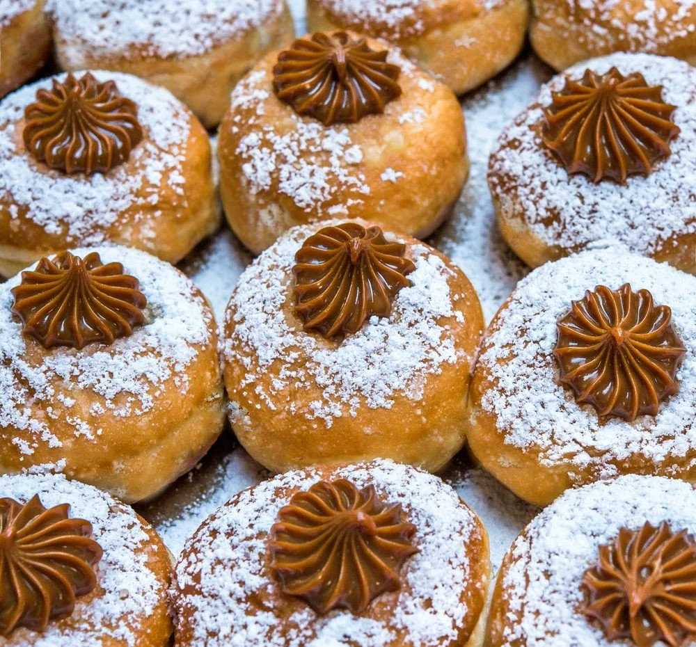 Varios sonhos cobertos com açúcar de confeiteiro e doce de leite 