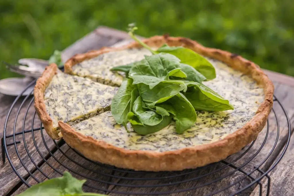 quiche de espinafre sobre uma grelha, em uma mesa de madeira rustica ao fundo uma vegetação.