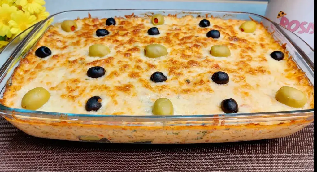 Refratário com bacalhau cremoso sobre uma mesa de madeira, do lado esquerdo flores amarelas 