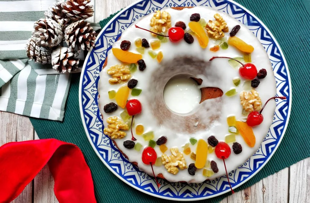 bolo de natal em um prato na cor branco com detalhes em azul ao lado pinhas.