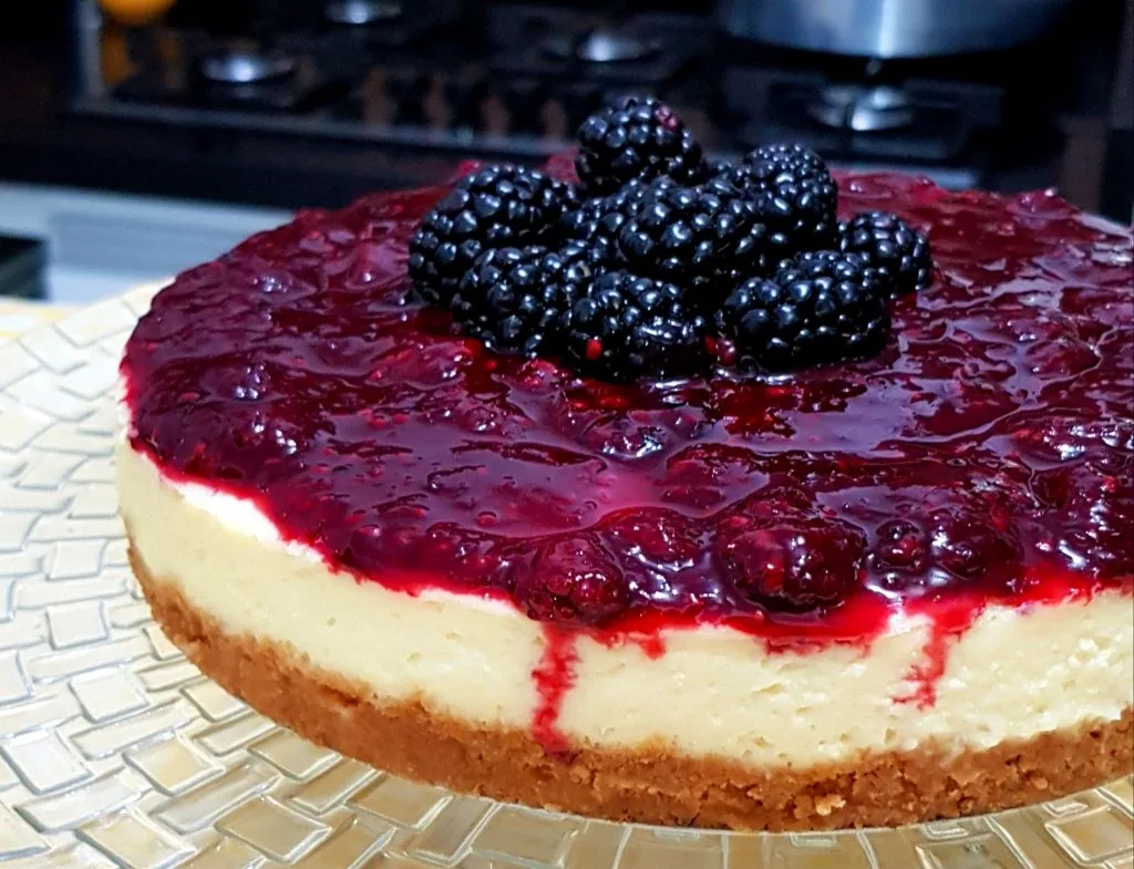 cheesecake de amora em um prato transparente ao fundo um fogão