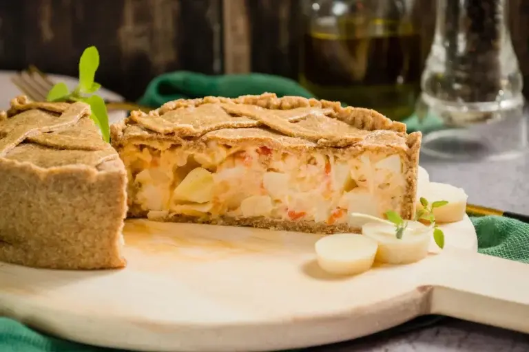 quiche de palmito sobre uma tabua de corte ao fundo um guardanapo verde e uma vasilha de óleo de oliva