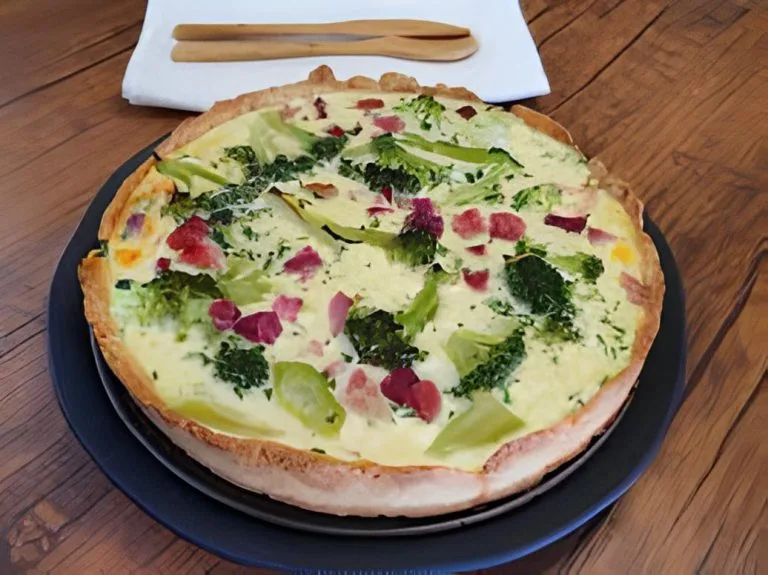 quiche de brócolis sobre um prato na cor escura sobre uma mesa de madeira rustica ao fundo uma tabua de corte e colheres de pau