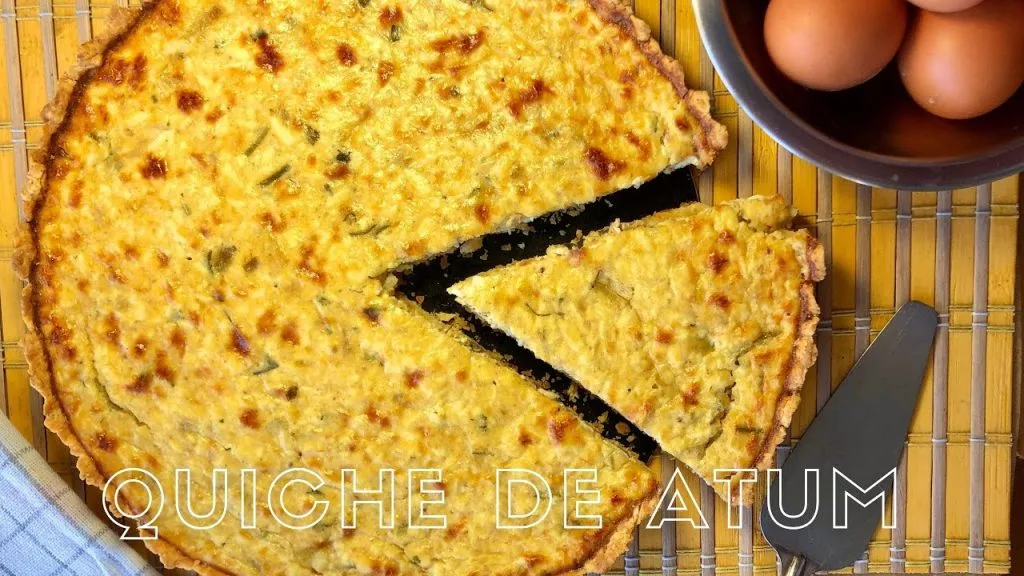 quiche de atum com uma fatia cortada ao lado uma espatula  e dois ovos sobre uma mesa de madeira