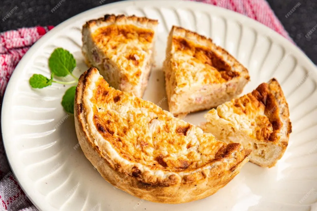 uma quiche de salmão sobre um prato branco ao lado da quiche uma rama de hortelã