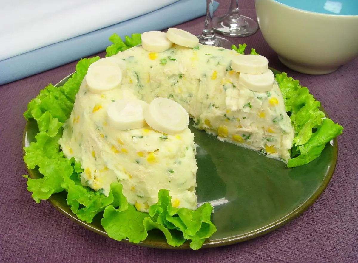 Maionese de batata com palmito em um prato na cor verde com folhas de alface em torno em uma mesa na cor marrom