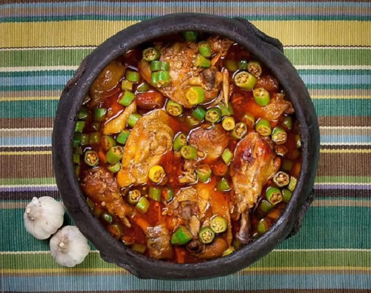 frango com quiabo em uma panela de barro sobre uma toalha listrada colorida