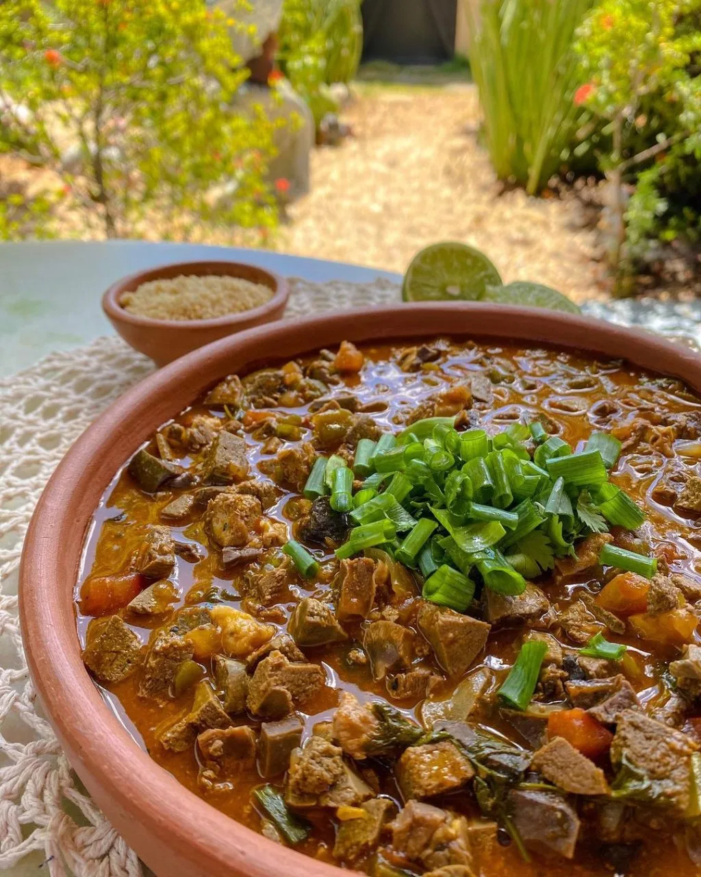 uma tigela de sarapatel sobre uma mesa na cor branca, ao fundo arvores 