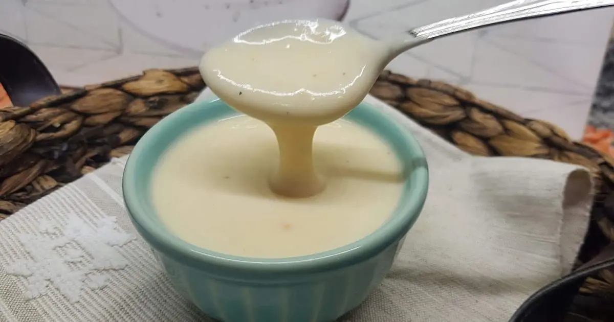 molho bechamel em uma cumbuca azul claro com uma colher retirando uma porção