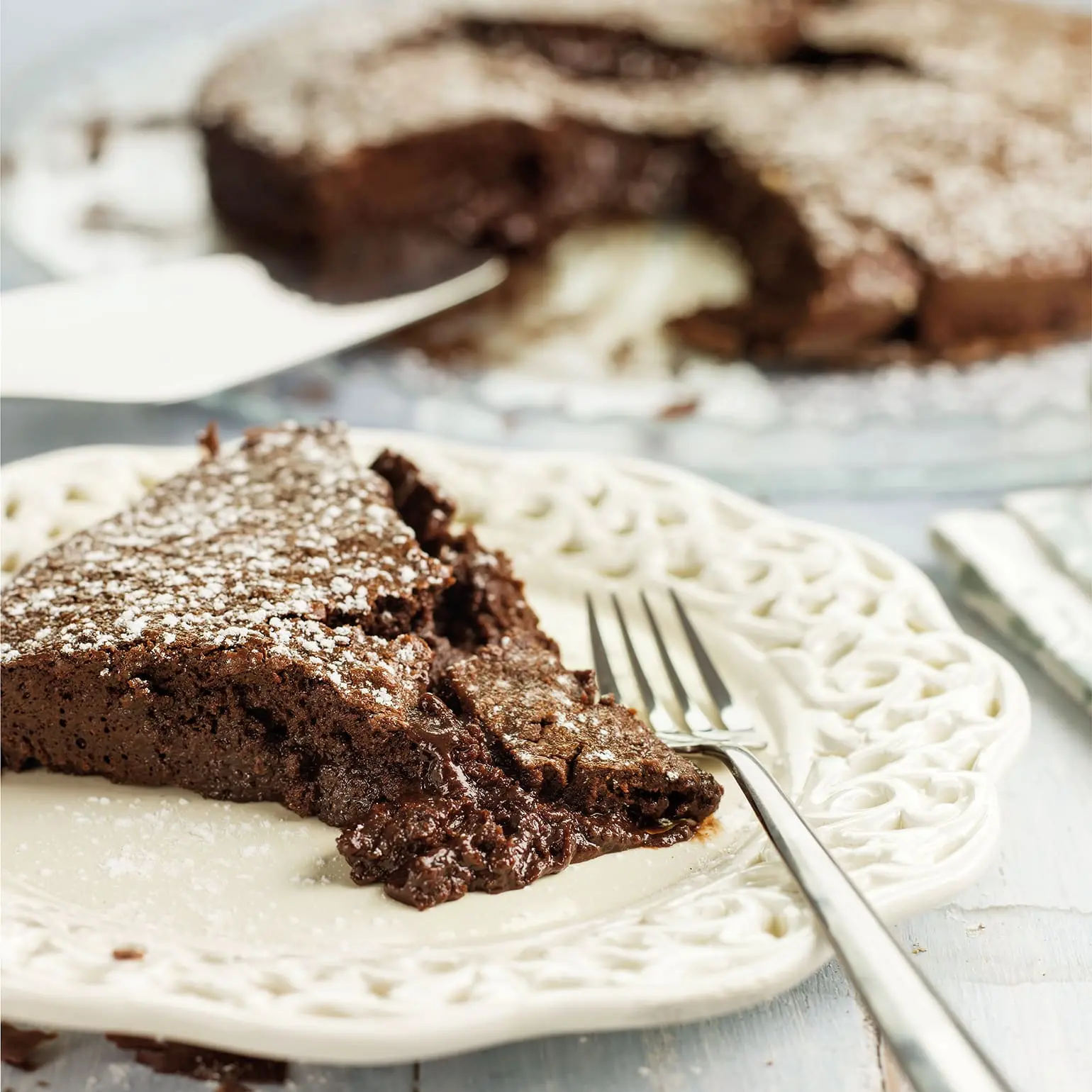 um prato com uma fatia de delicia de chocolate junto ao garfo de sobremesa ao fundo o restante da delicia