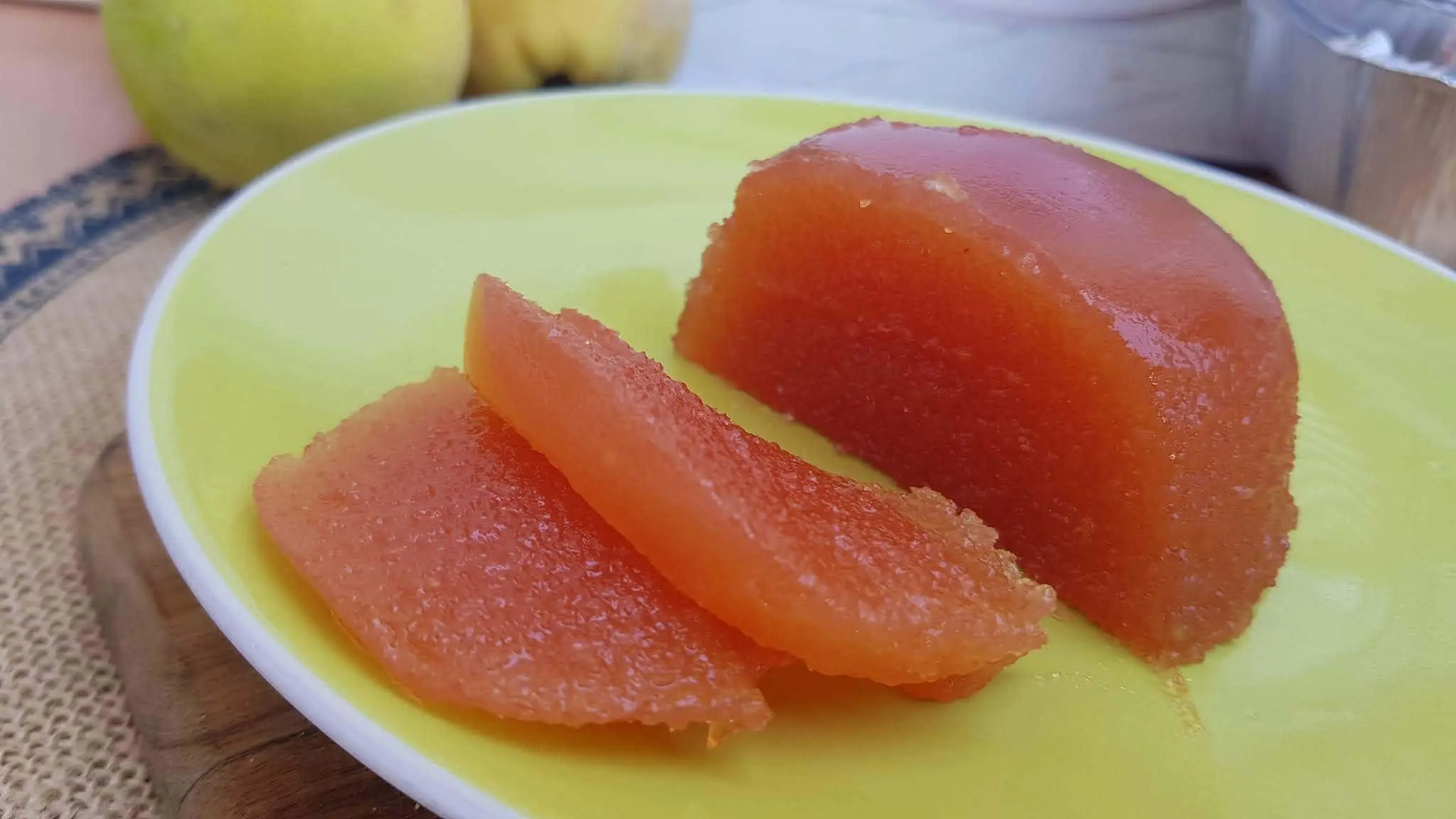 marmelada em um prato amarelo com marmelos ao fundo