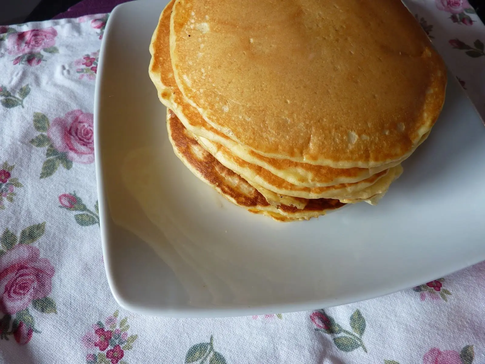 pilha de panquecas em um prato branco sobre uma toalha florida