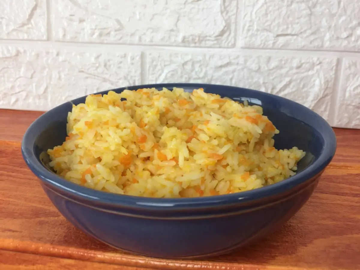 Arroz com cenoura em uma tigela na cor azul sobre uma mesa de madeira