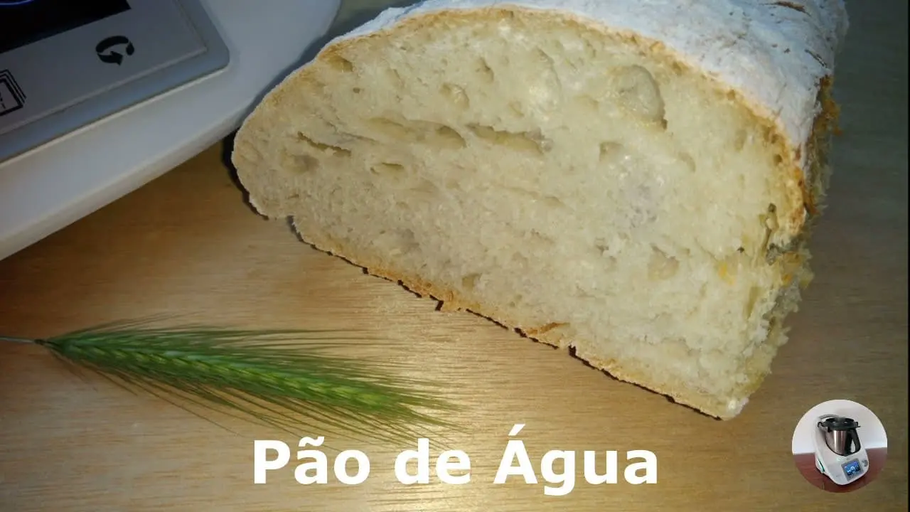 pão sobre uma tabua de corte, ja com uma fatia retirada com uma bimby ao fundo