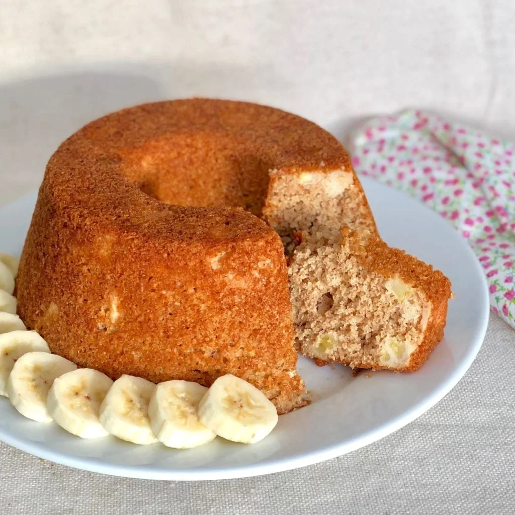 bolo de banana  em um prato branco com bananas ao lado.