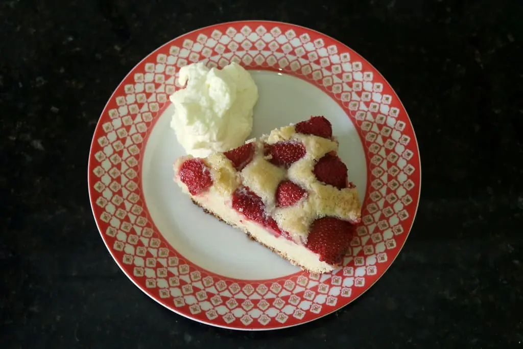 uma fatia de bolo de morango em um prato branco com detalhes em vermelho