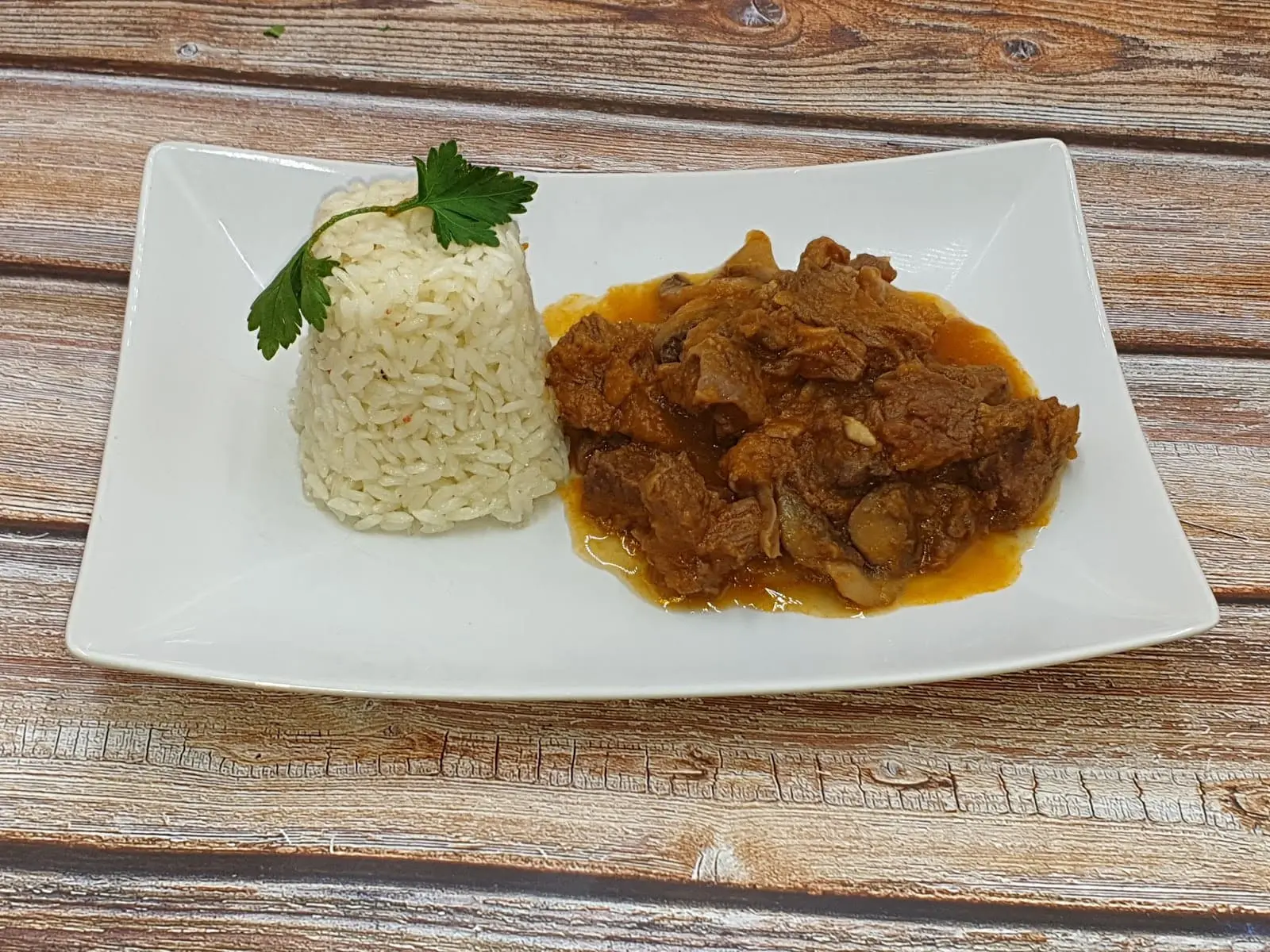 carne estufada com uma porção de arroz em um prato branco retangular