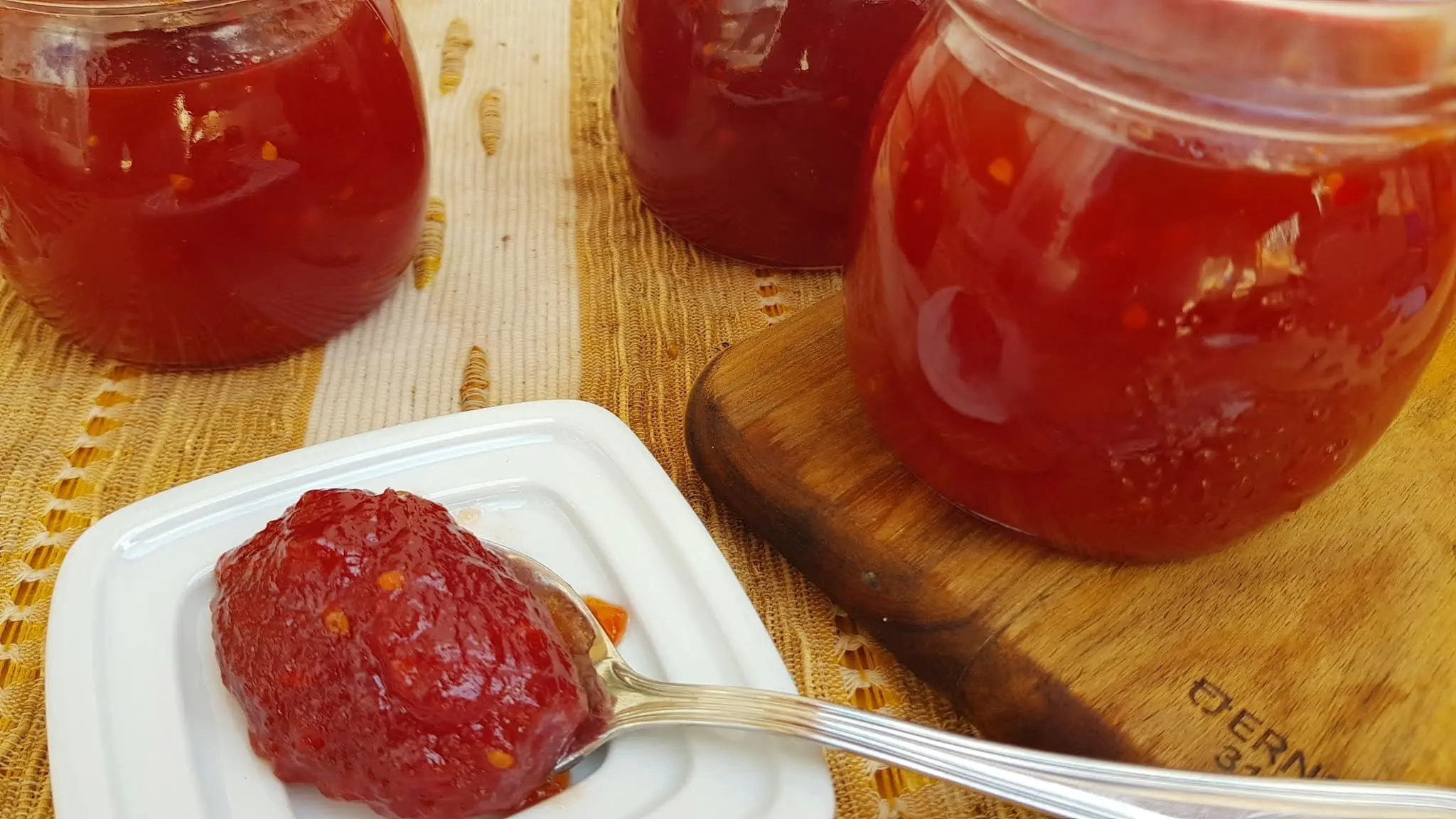 potes de doce de tomate ao lado uma colher com uma porção de doce sobre uma tampa na cor branca