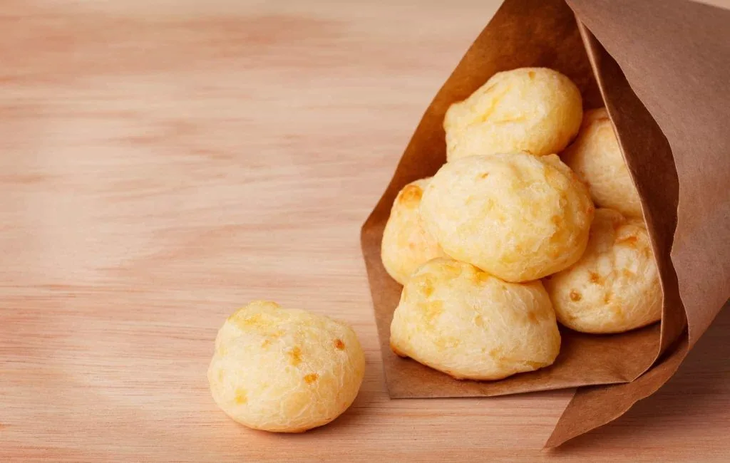 Pães de queijo em saco de papel sobre uma mesa de madeira