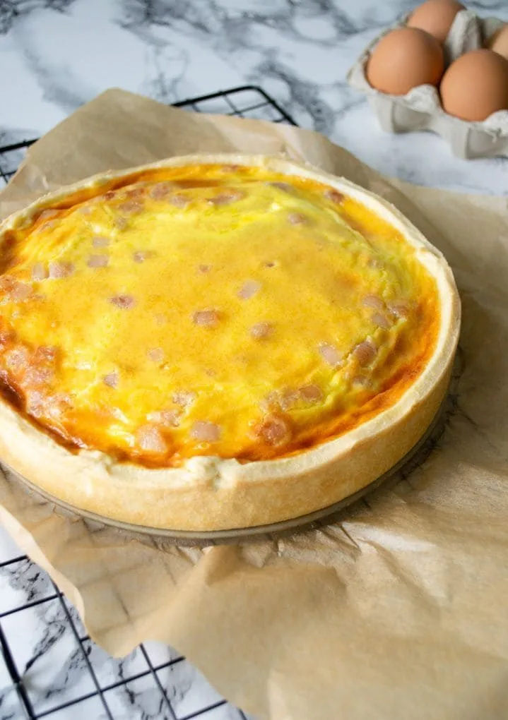 quiche sobre um papel manteiga com ovos ao fundo