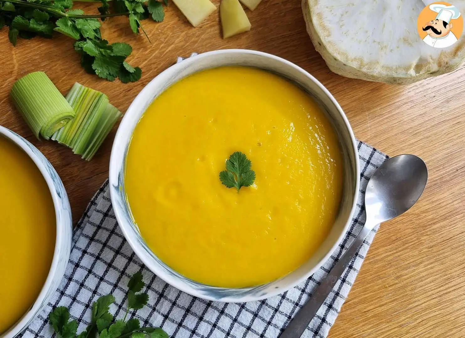 sopa de legumes em uma tigela branca sobre uma toalha quadriculada nas cores branca e azul, ao redor ingredientes da sopa