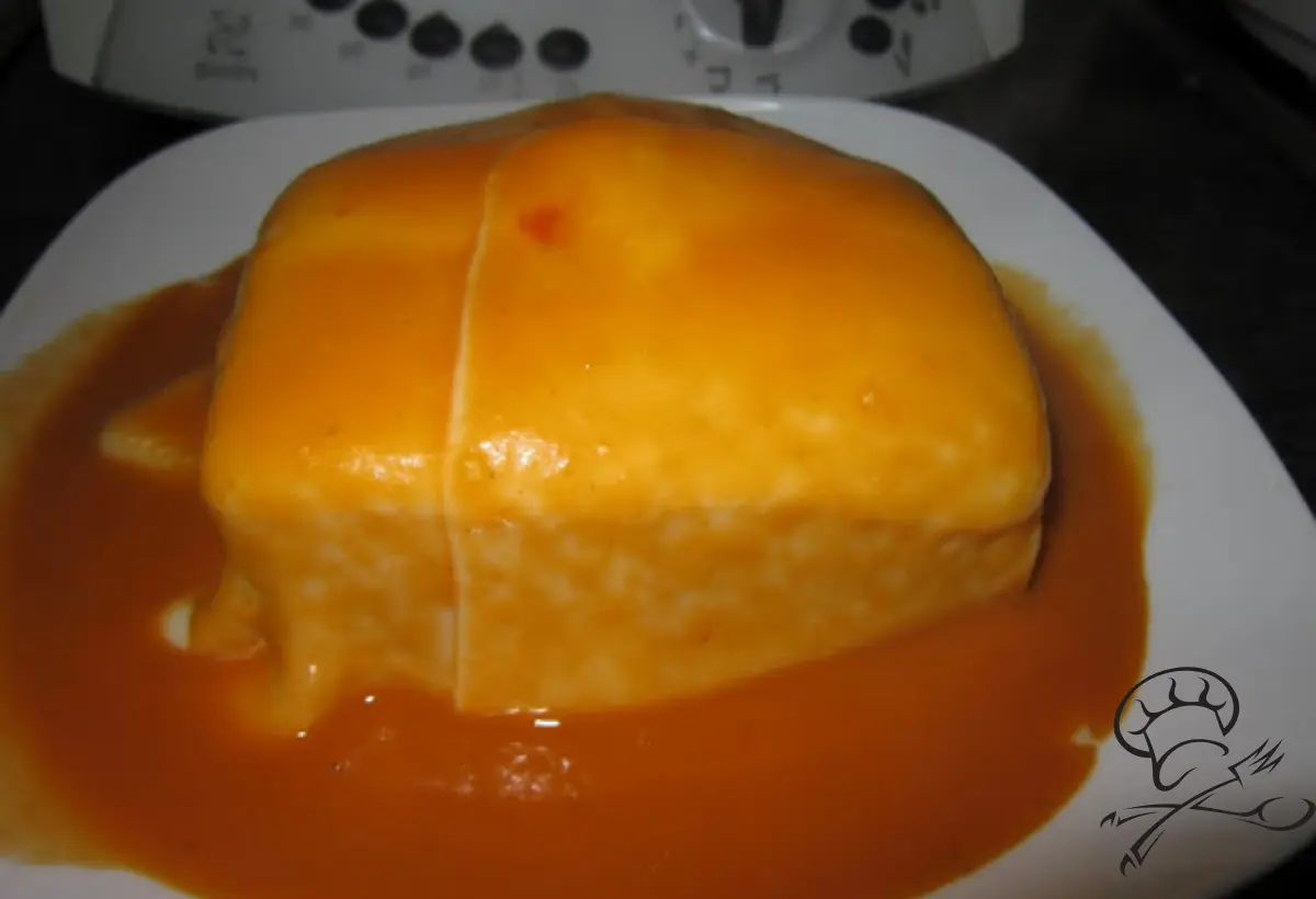 Francesinha em prato branco com uma bimby ao fundo