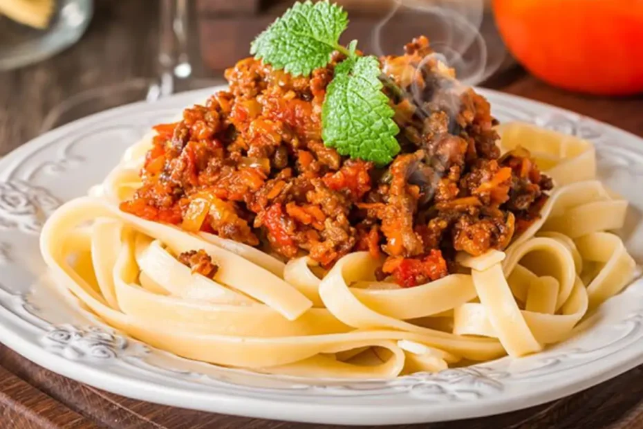 macarrão com carne moída em um prato branco com uma taça ao fundo