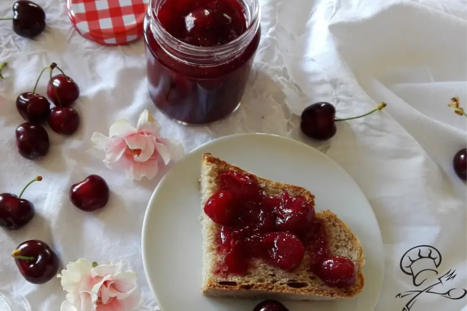 um vidro com doce de cereja ao lado um prato com uma fatia de pães com o doce com cerejas em torno