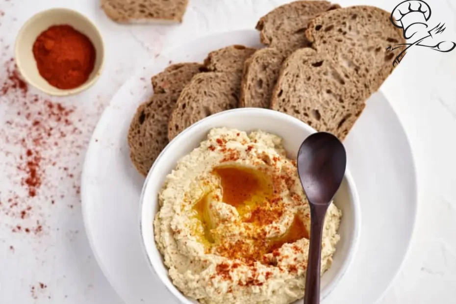 hummus em uma tigela branca ao lado fatias de pão