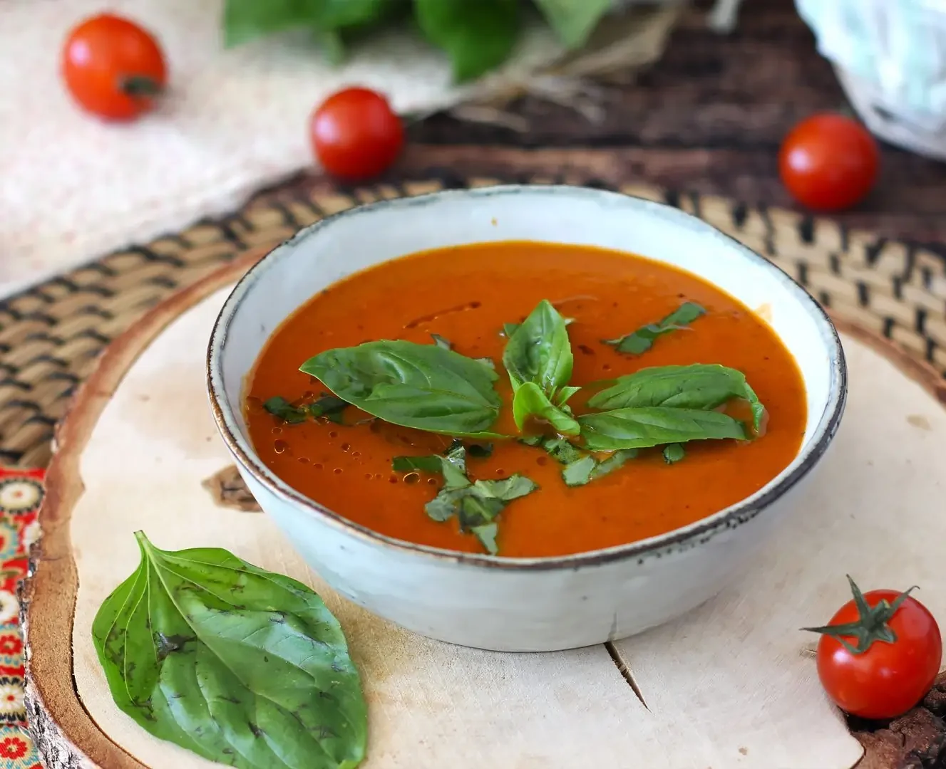 sopa de tomate em uma cumbuca na cor branca com alguns tomates em volta da tigela